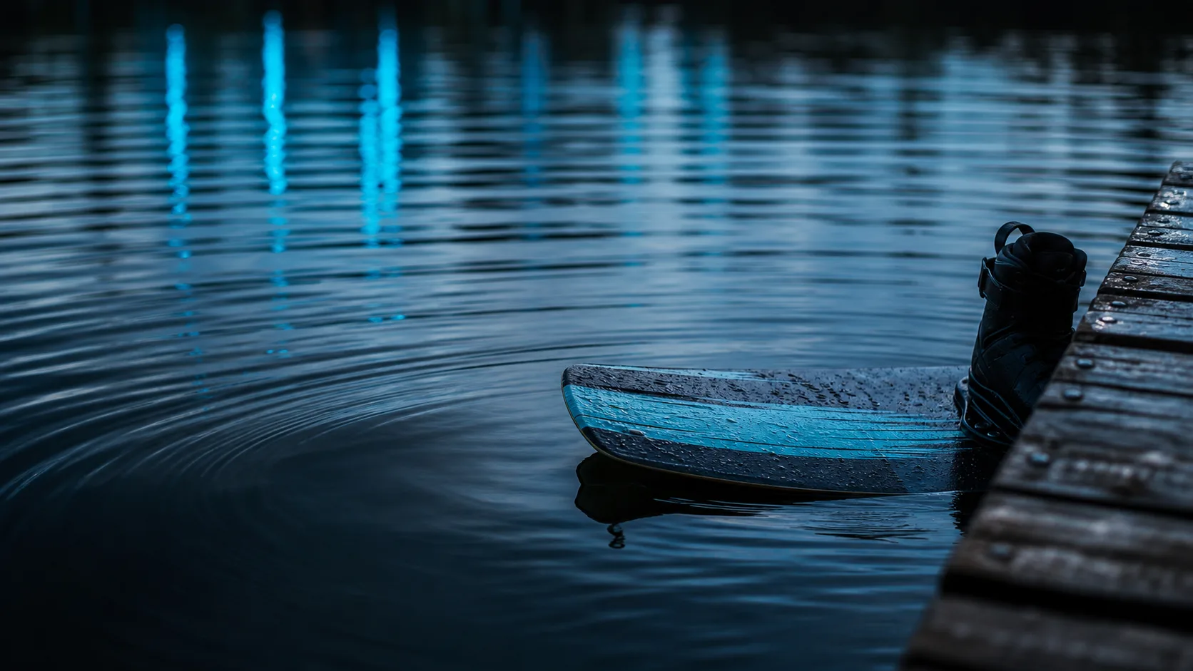 Prancha de wakeboard parcialmente visível sobre água escura com ondas suaves e reflexos em azul