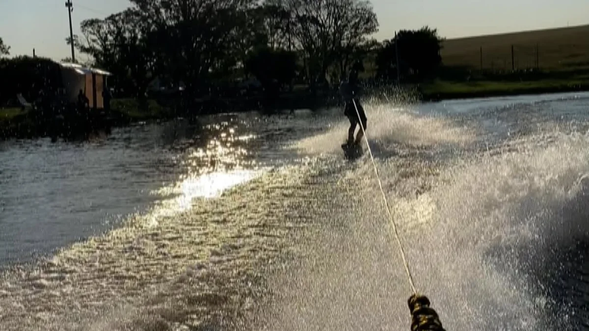 Rider de wakeboard no lago do Coxilha Cable Park, com cabo e área rural ao fundo