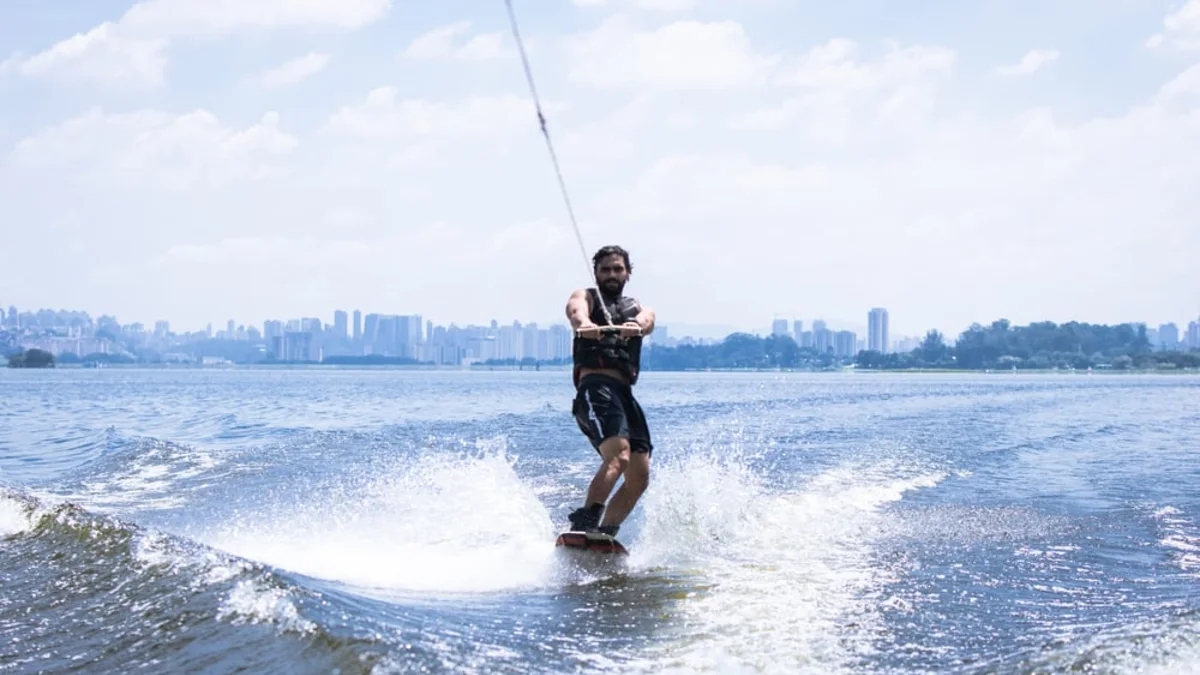 Rider de wakeboard puxado por barco na Represa Guarapiranga, com São Paulo ao fundo