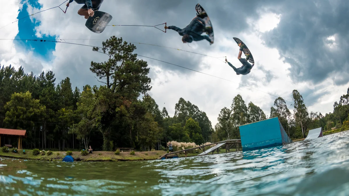 Rider de wakeboard em salto sobre o lago do Royal Wake Park, com kicker e cabo visíveis